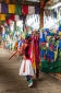 Soldier In traditional costume on covered bridge by market with prayer flags, Thimphu, Western Bhutan