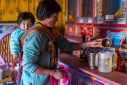 Farmwife with grandson on her back prepares the family Buddhist shrine for the day at her home in Phobjikha Valley, Western Bhutan.
