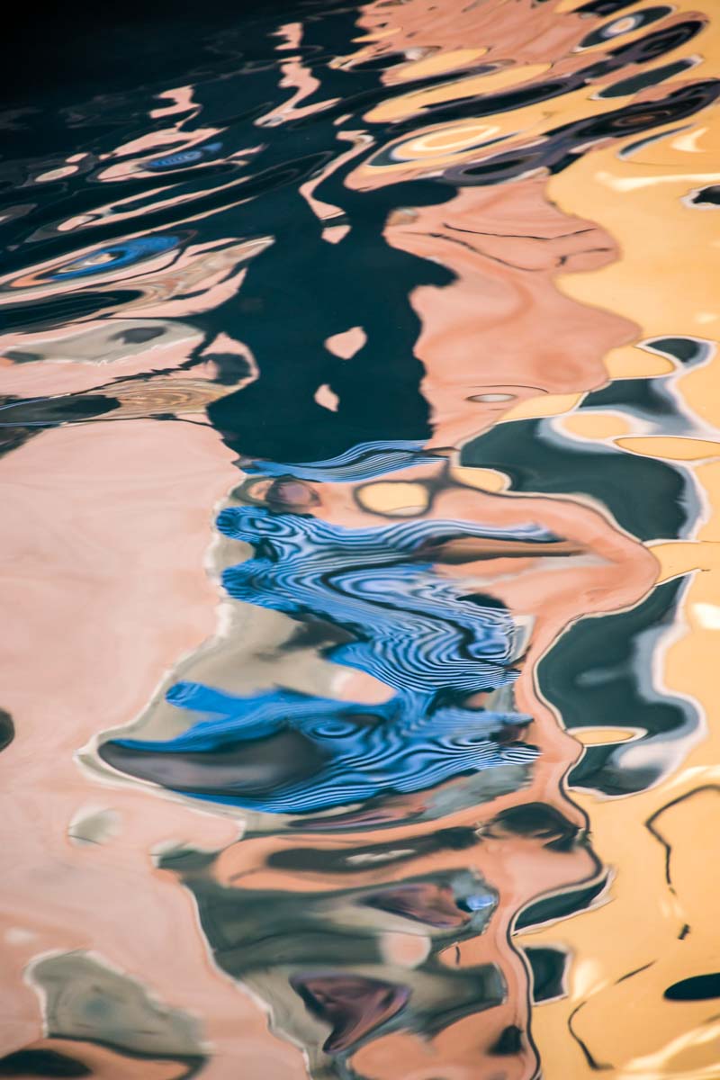 Reflection of a gondolier in a pink and gold canal in Venice